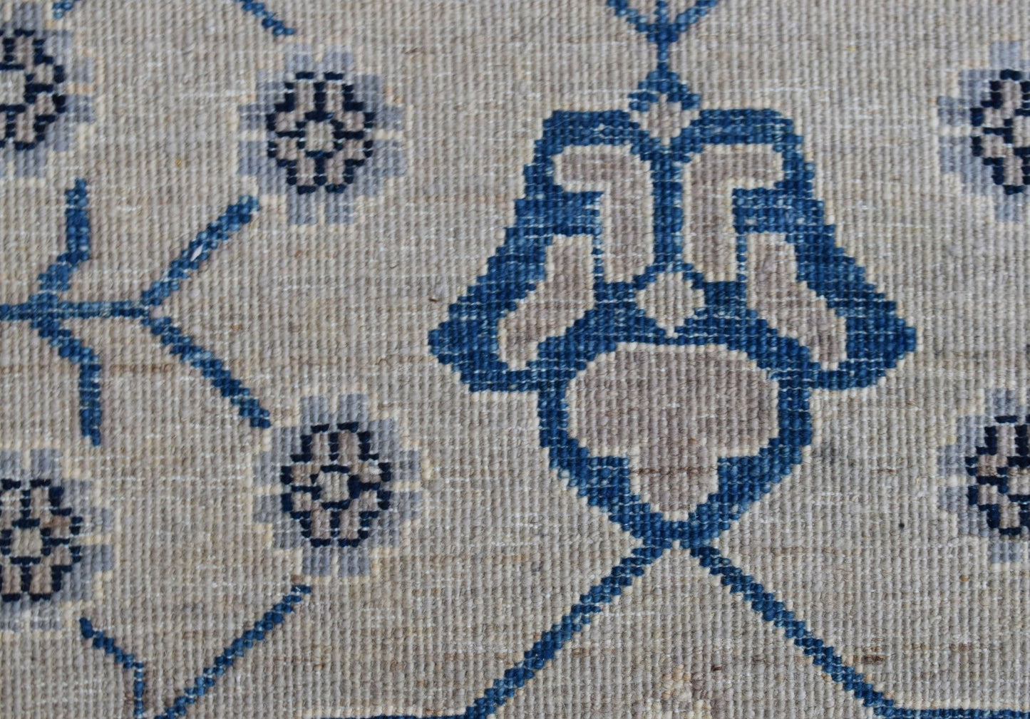 A close-up of an Afghan Chobi rug featuring a blue geometric floral pattern on a beige wool base.