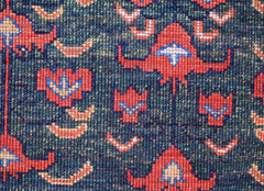 A close-up of a handwoven Afghan Chobi rug featuring intricate geometric red and blue patterns.