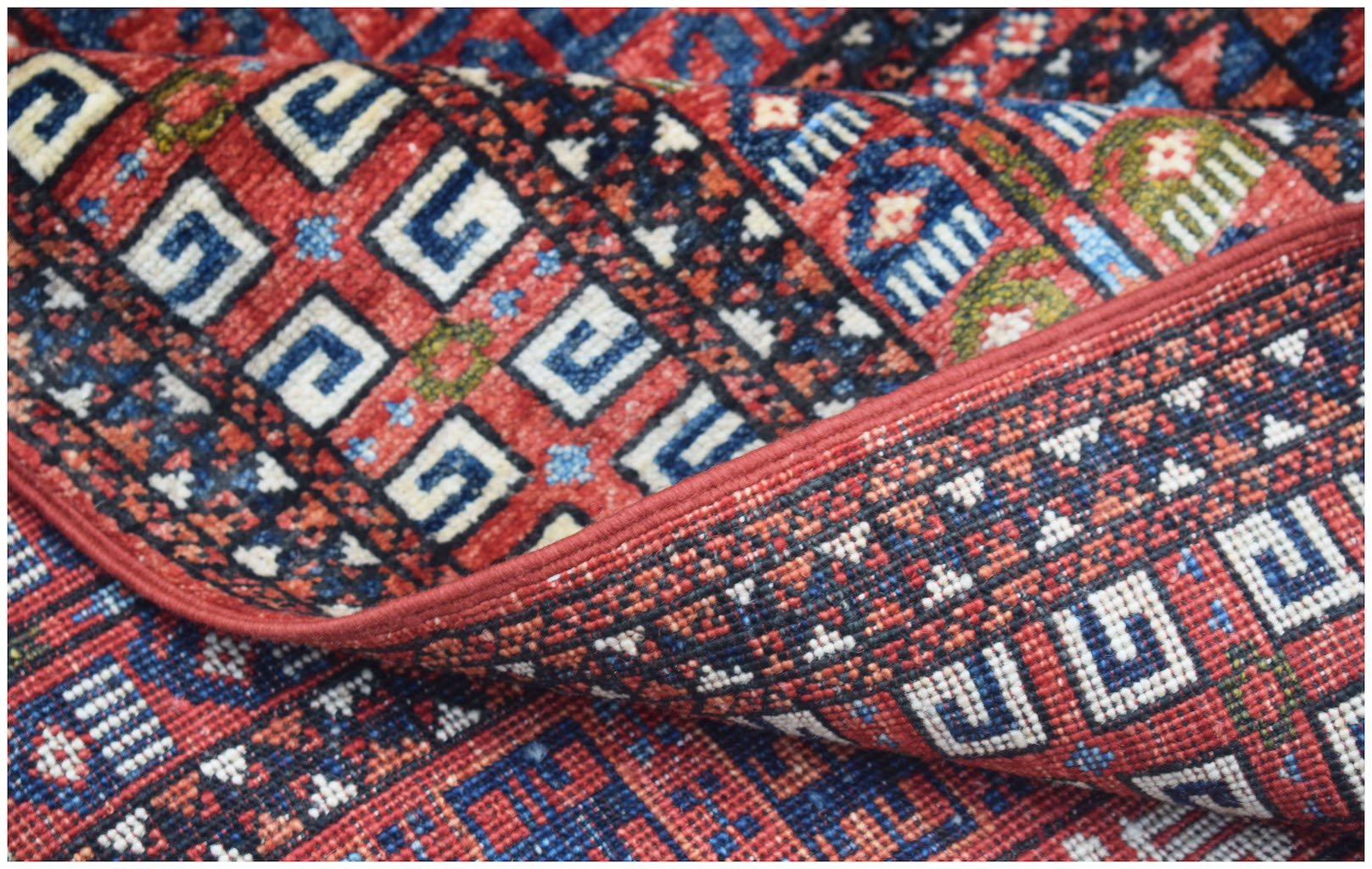 A handmade Afghan Chobi rug featuring a geometric pattern in red, blue, and ivory wool.
