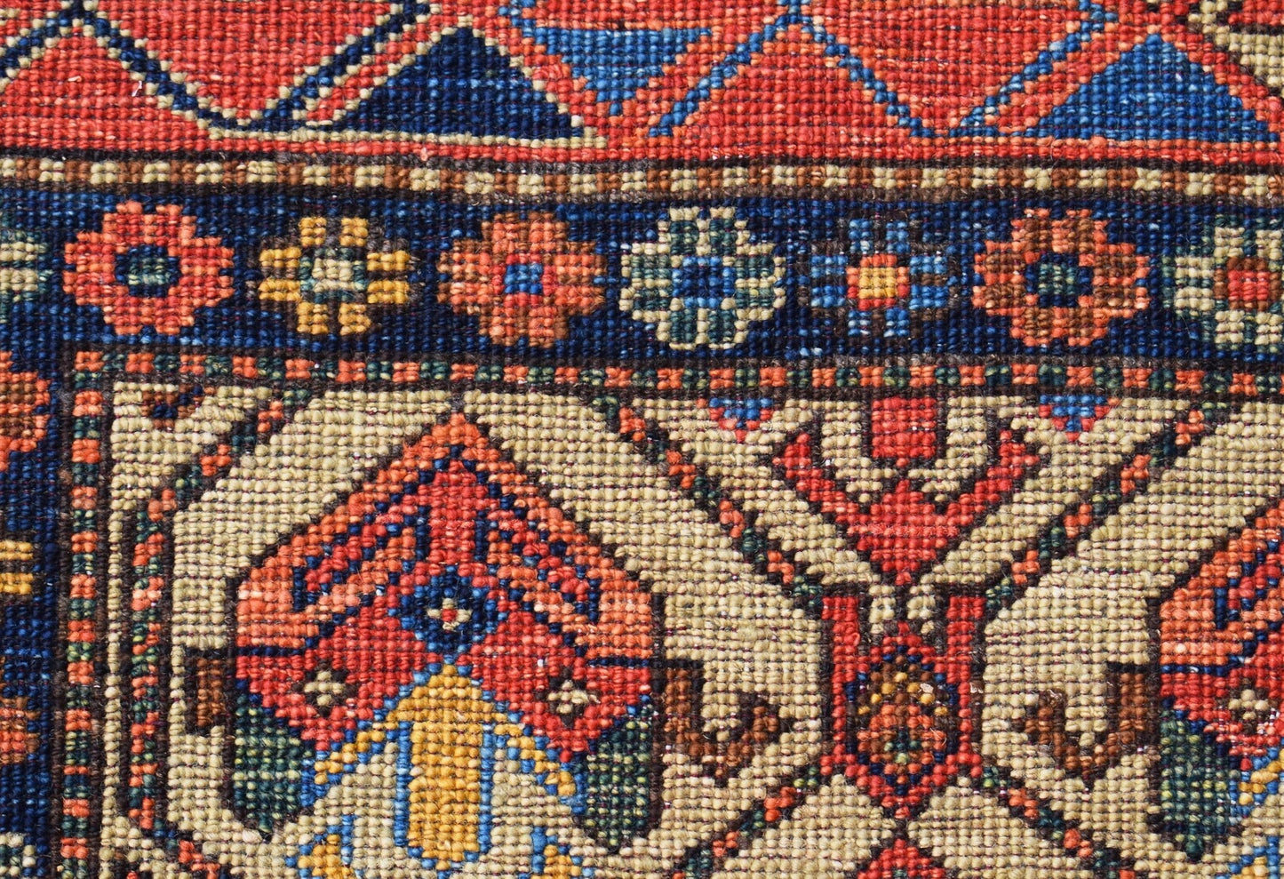 A close-up of an Afghan Chobi rug featuring intricate geometric patterns in red, blue, and ivory.