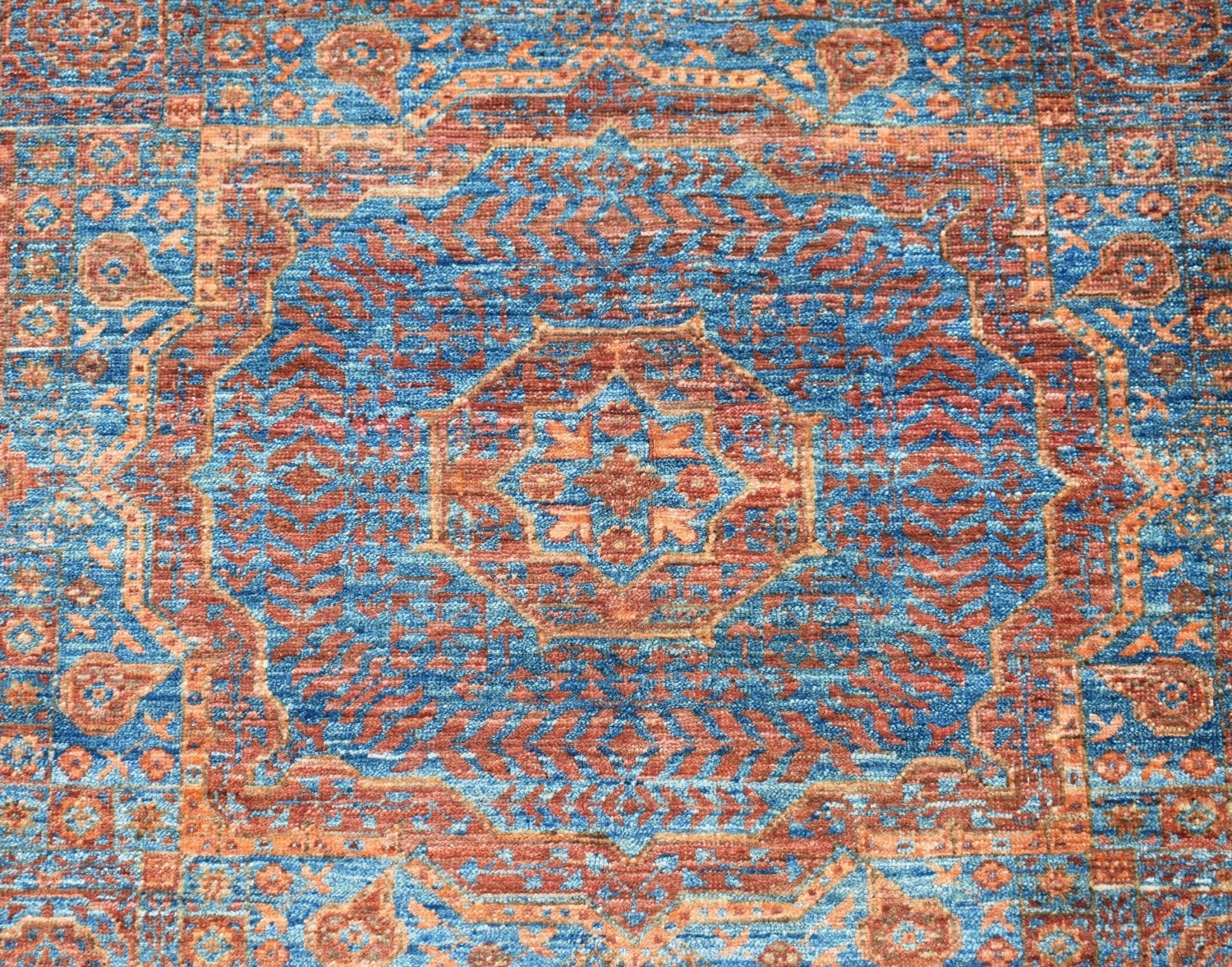 A handmade Afghan Chobi rug featuring a detailed blue and rust-colored Mamluk medallion pattern.