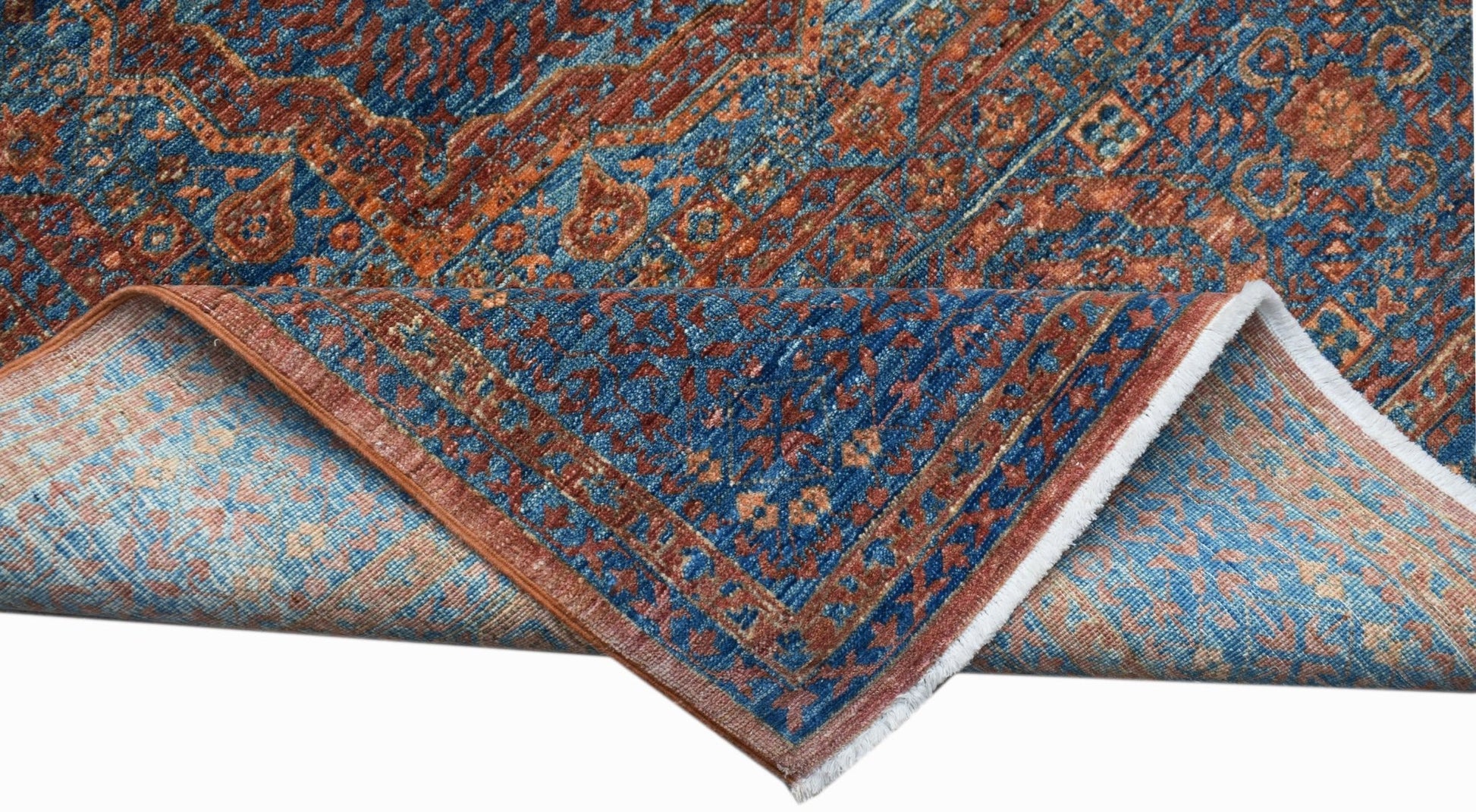 A handwoven Afghan Chobi rug with a blue and rust Mamluk pattern shown folded to reveal the back.
