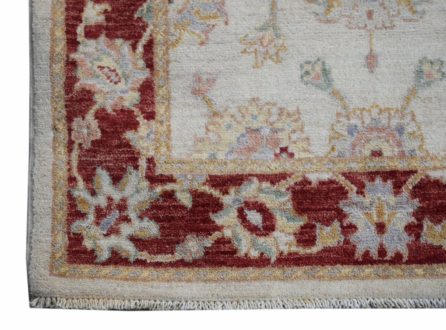 A handmade Afghan Chobi rug featuring a cream field with a red floral border and fringe.