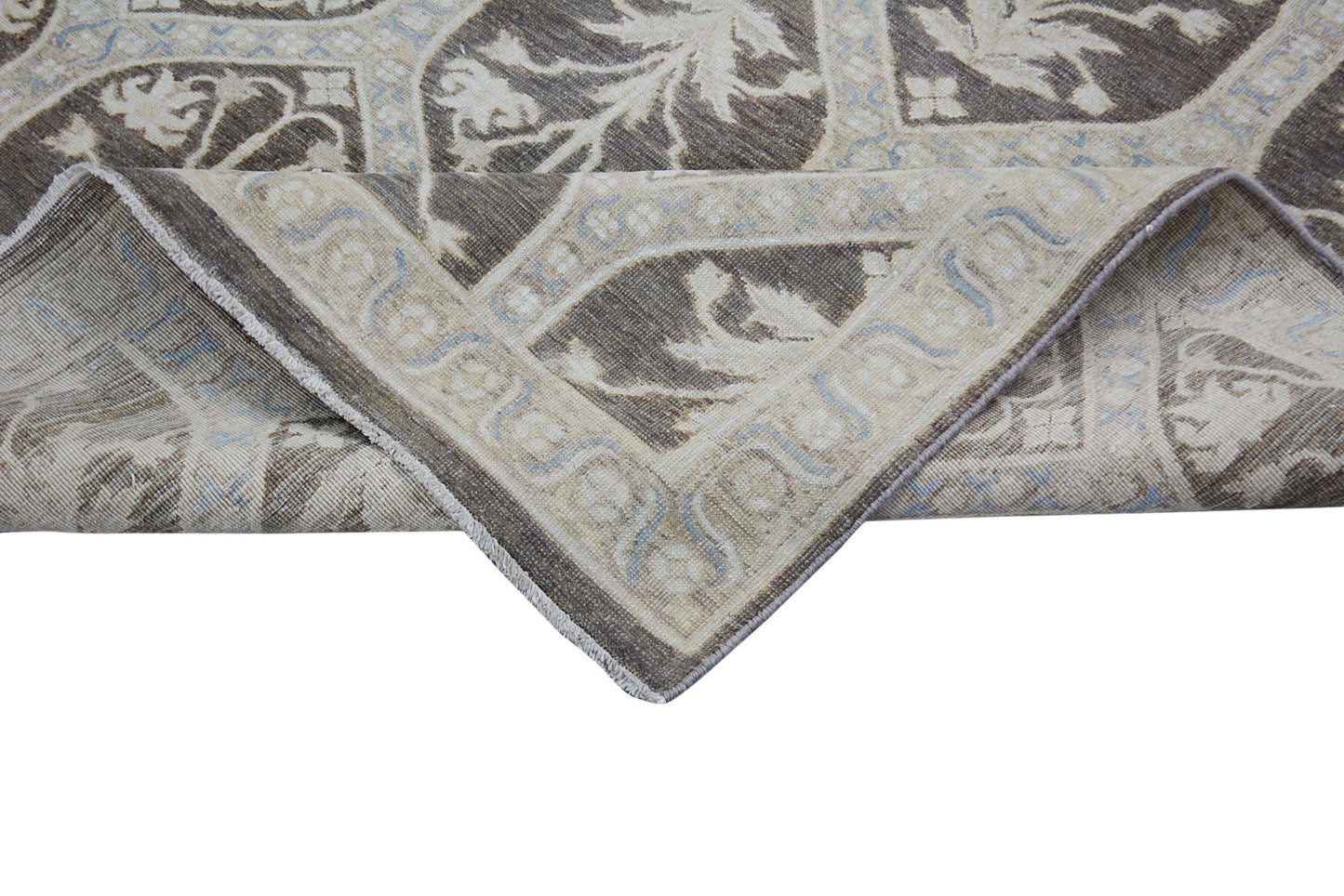 A corner of a handmade Afghan Chobi rug featuring a brown and beige floral pattern.