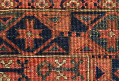 A close-up of a handwoven Afghan Chobi rug featuring geometric patterns in earthy red and blue tones.