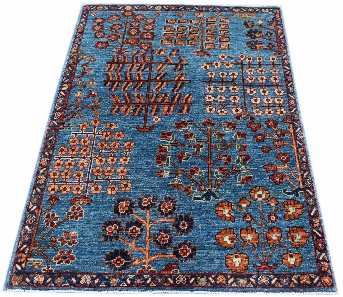Handmade Afghan Chobi rug featuring a blue field with stylized floral and tree motifs.