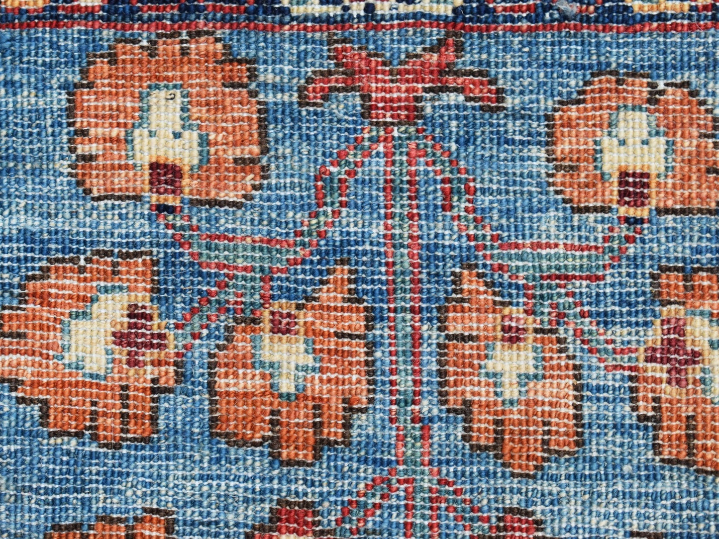 A close-up of a handwoven Afghan Chobi rug featuring orange floral motifs on a blue background.