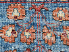A close-up of a handwoven Afghan Chobi rug featuring orange floral motifs on a blue background.