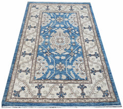 A rectangular Afghan Chobi rug featuring a blue central medallion and floral patterns on cream.