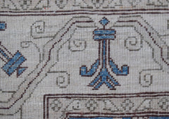 A close-up of an Afghan Chobi rug featuring intricate blue and brown floral motifs on a cream base.