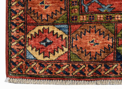 A close-up of an Afghan Chobi rug featuring geometric medallions in earthy tones on a red field.