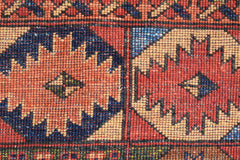 A close-up of a handwoven Afghan Chobi rug featuring geometric medallions in red, blue, and tan.