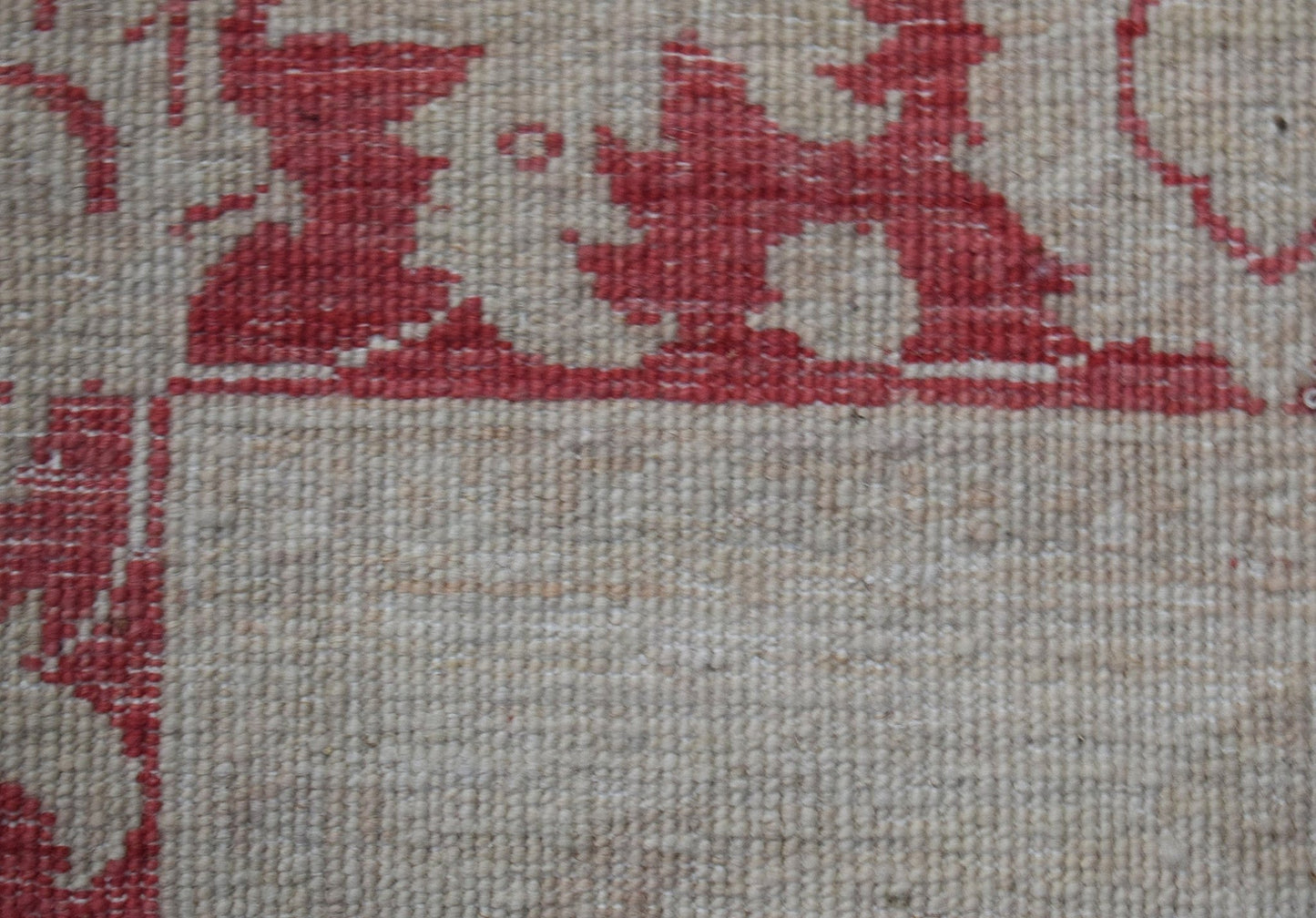 A close-up of a handwoven Afghan Chobi rug featuring a red floral pattern on a beige wool field.
