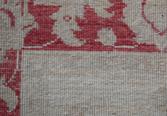 A close-up of a handwoven Afghan Chobi rug featuring a red floral pattern on a beige wool field.