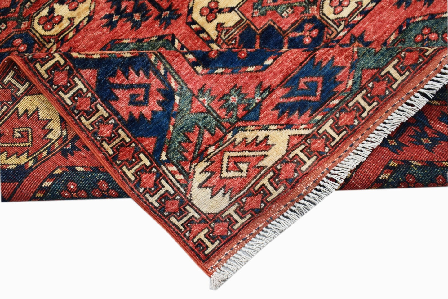 A folded Afghan Chobi rug featuring traditional geometric patterns in red, blue, and cream wool.