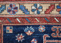A close-up of a handwoven Afghan Chobi rug featuring geometric floral patterns in blue and red.