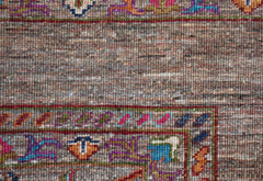 A close-up of a handwoven Afghan Chobi rug featuring a textured brown field and colorful borders.