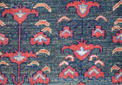 A close-up of an Afghan Chobi rug featuring a repeating floral pattern in red and blue on green.