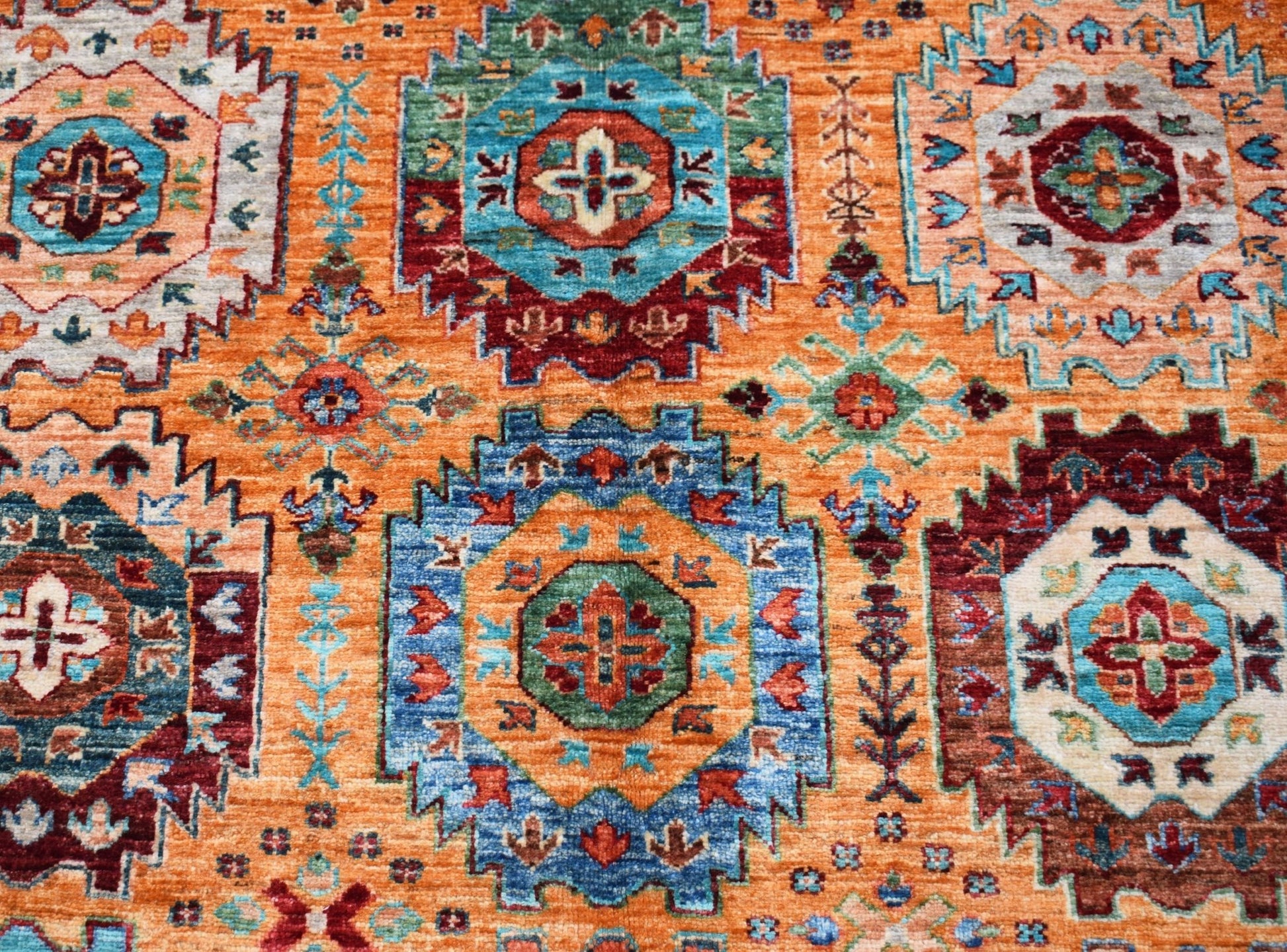 An Afghan Chobi rug featuring a vibrant orange field with intricate geometric medallion patterns.