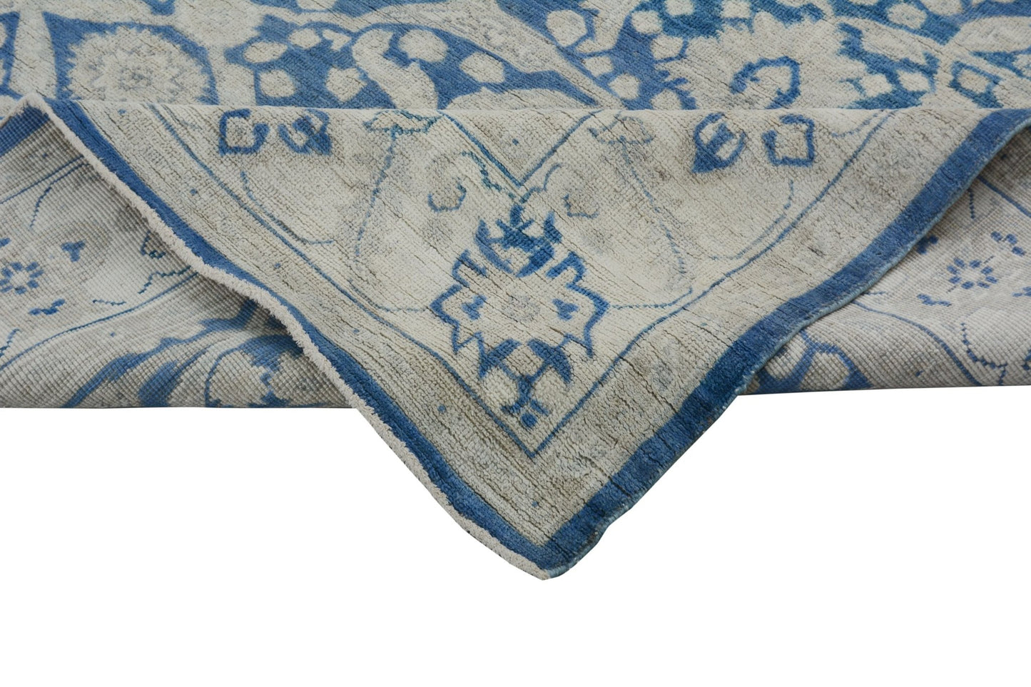 A handmade Afghan Chobi rug featuring a blue and cream floral pattern with a folded corner.