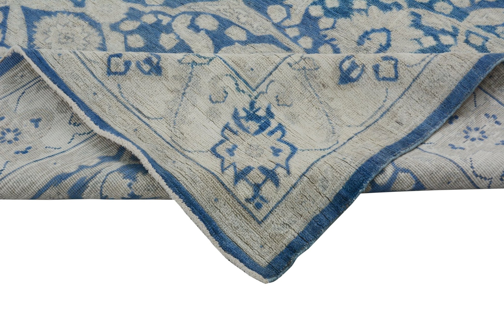 A handmade Afghan Chobi rug featuring a blue and cream floral pattern with a folded corner.