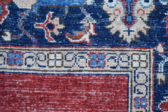 A close-up of a handwoven Afghan Chobi rug featuring a red field and a blue floral border.