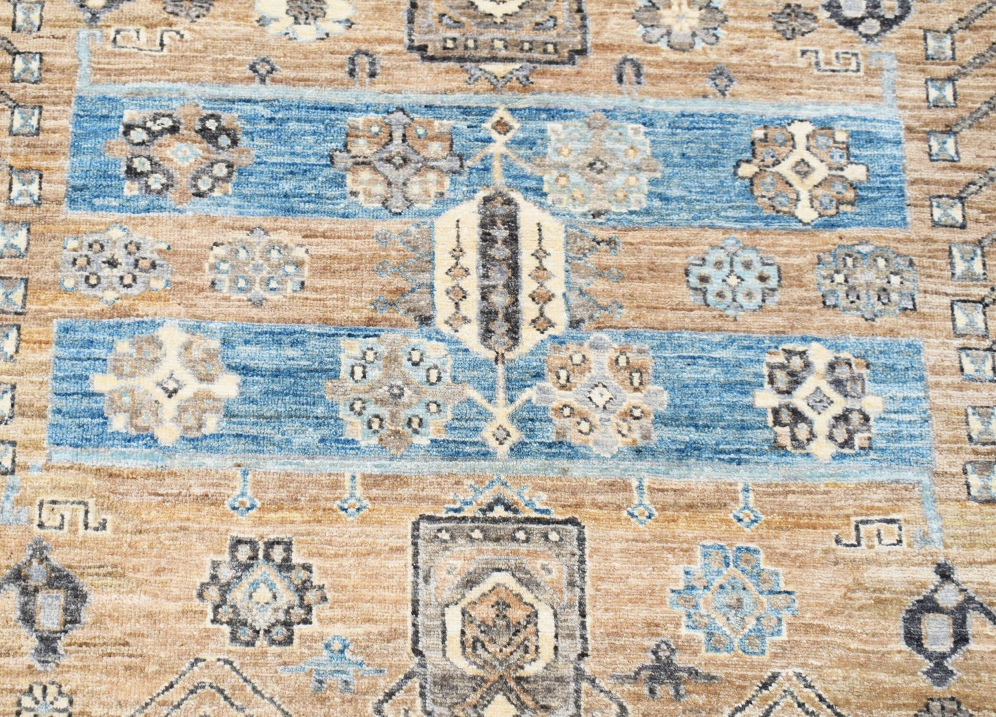 A handwoven Afghan Chobi rug featuring geometric floral motifs in blue and earthy brown tones.