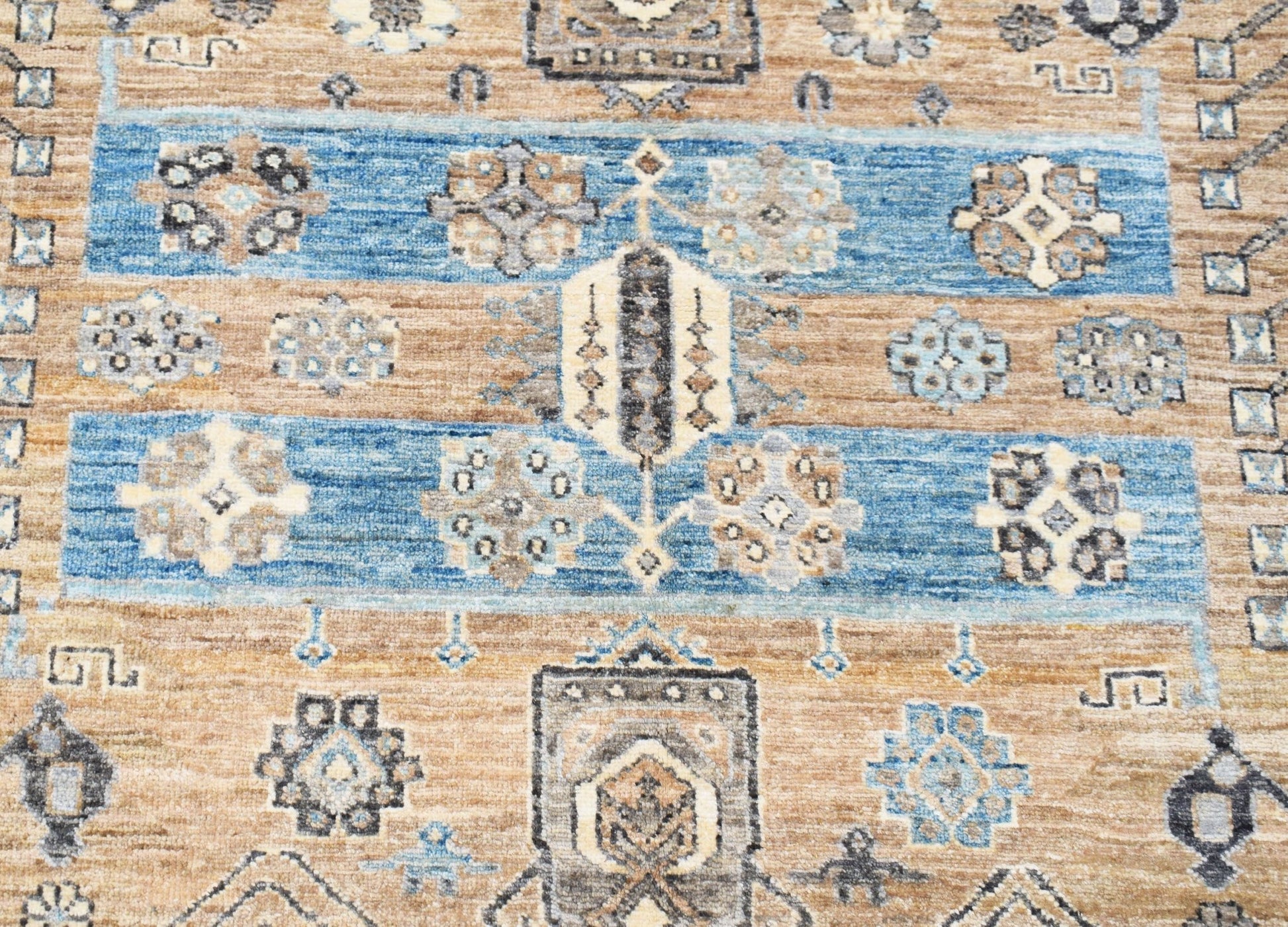 A handwoven Afghan Chobi rug featuring geometric floral motifs in blue and earthy brown tones.