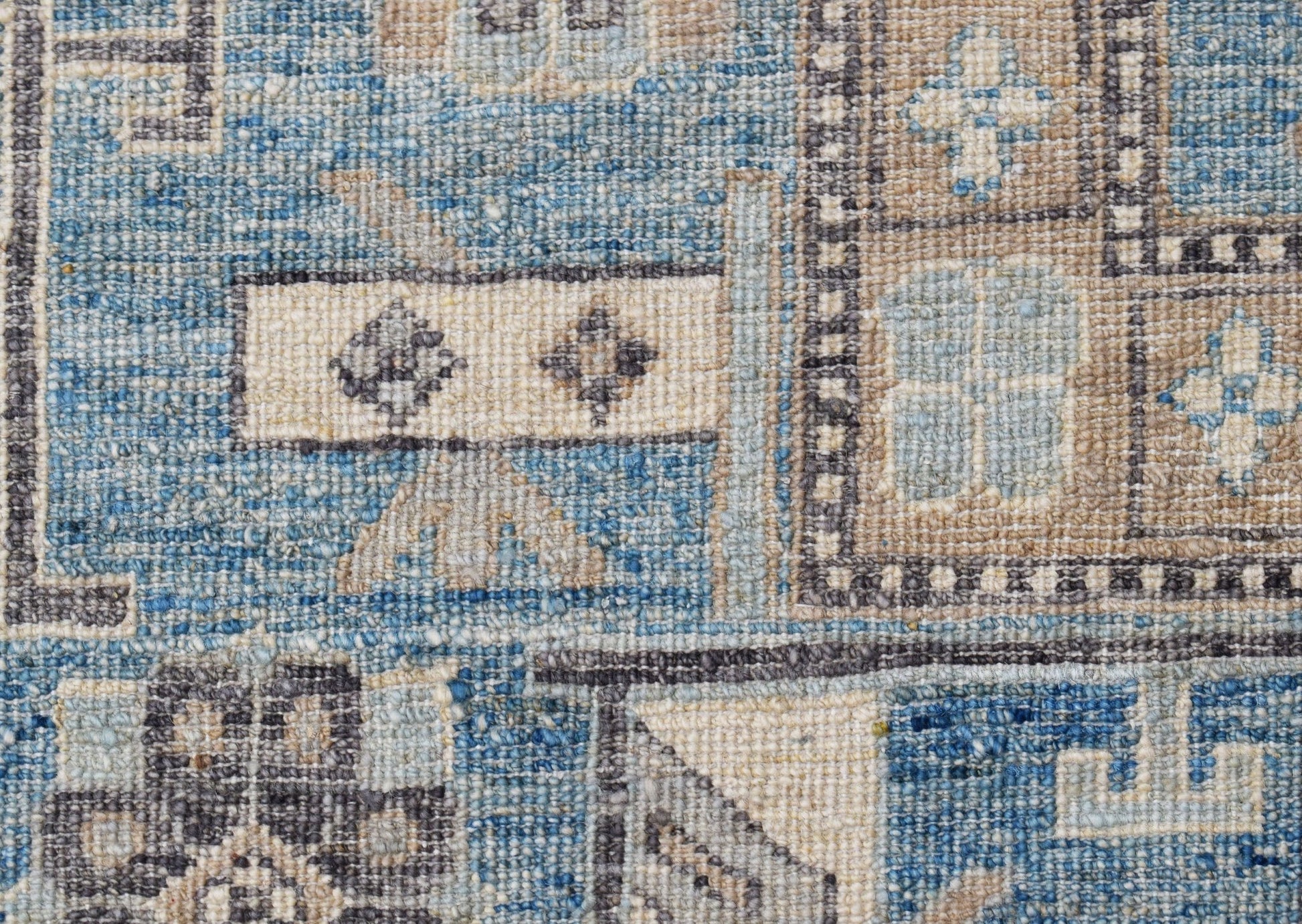 A close-up of a handwoven Afghan Chobi rug featuring geometric patterns in blue and beige tones.