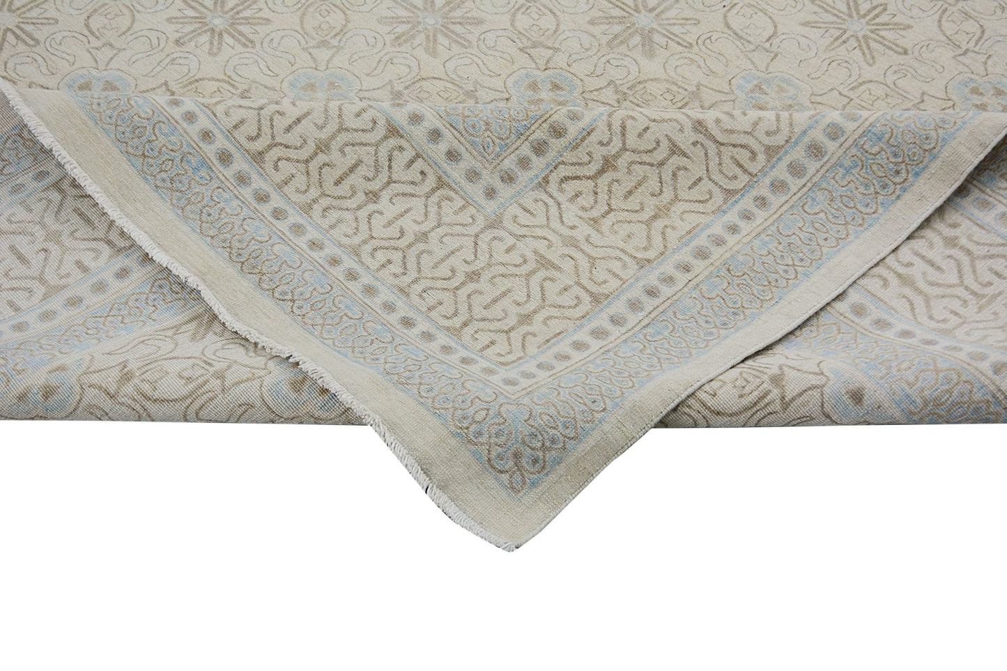 An Afghan Chobi rug with a beige and light blue geometric pattern, shown folded at the corner.