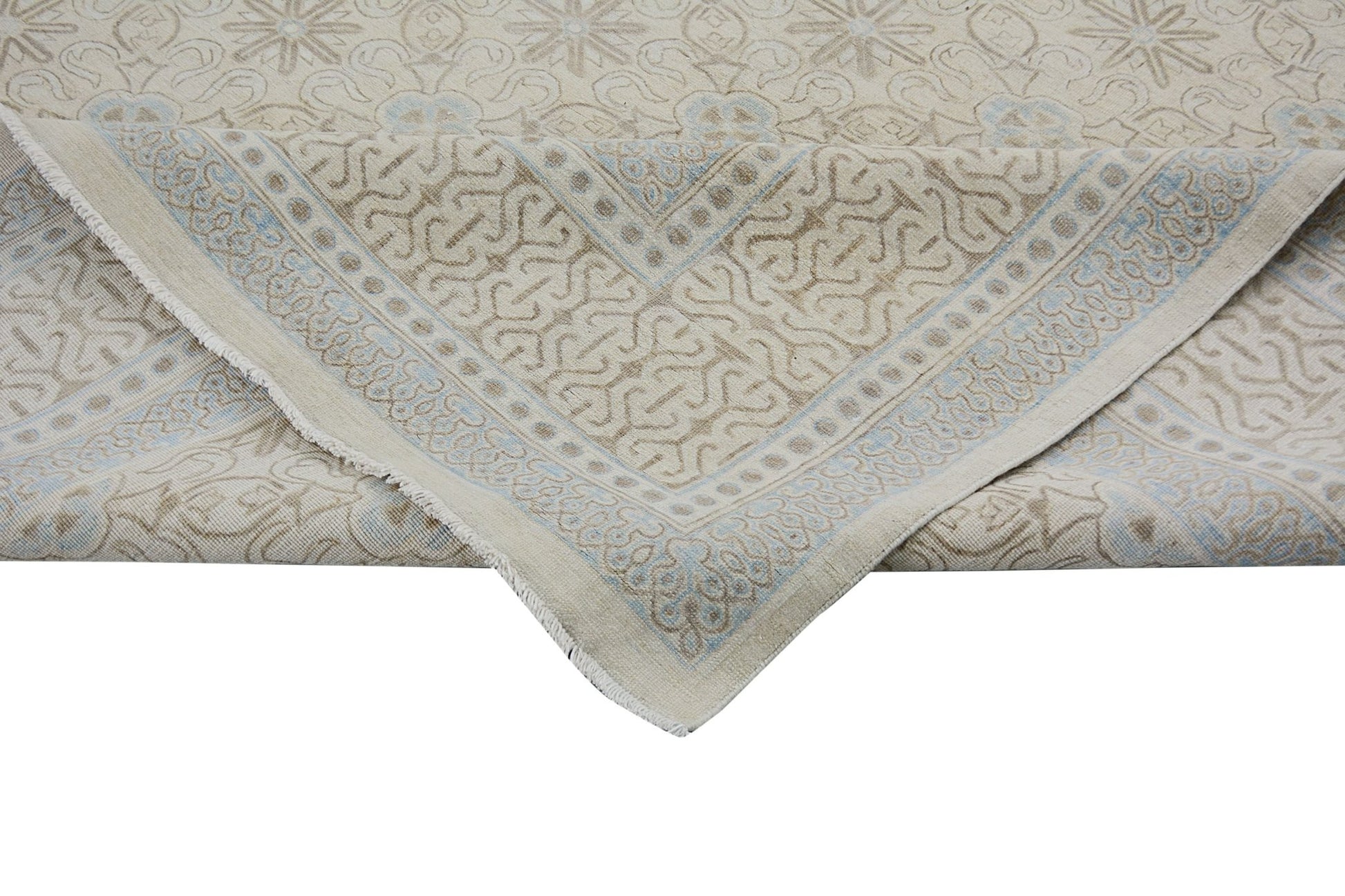 An Afghan Chobi rug with a beige and light blue geometric pattern, shown folded at the corner.