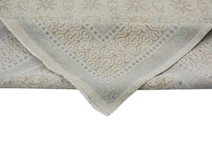 An Afghan Chobi rug with a beige and light blue geometric pattern, shown folded at the corner.