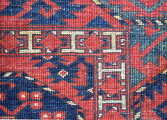 A close-up of a handwoven Afghan Chobi rug featuring a geometric border pattern in red and blue.