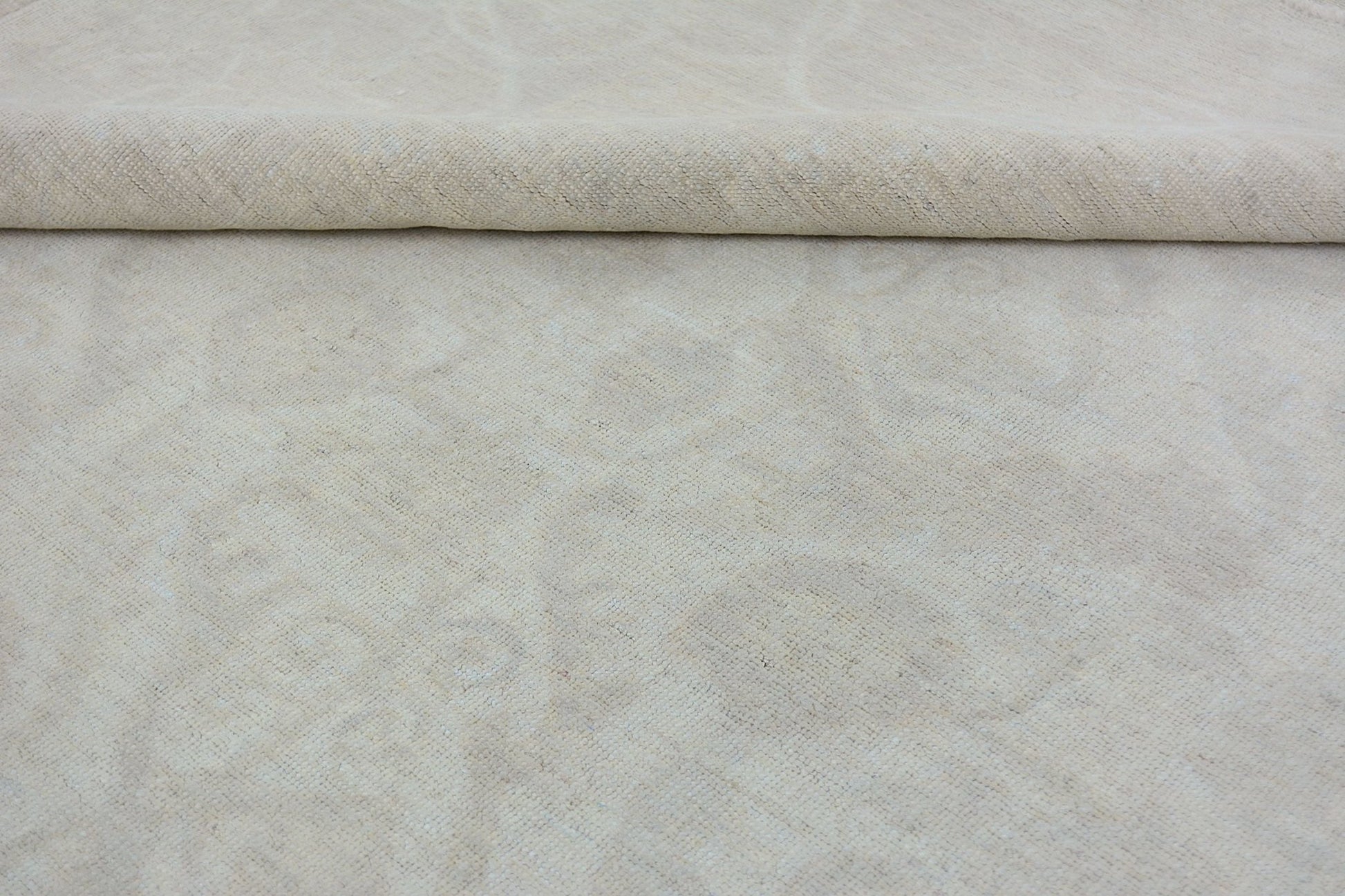 A handmade Afghan Chobi rug featuring a subtle, monochromatic cream-colored floral pattern.