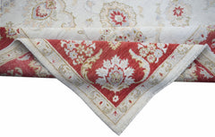A handwoven Afghan Chobi rug with a cream field and a red floral border folded at the corner.