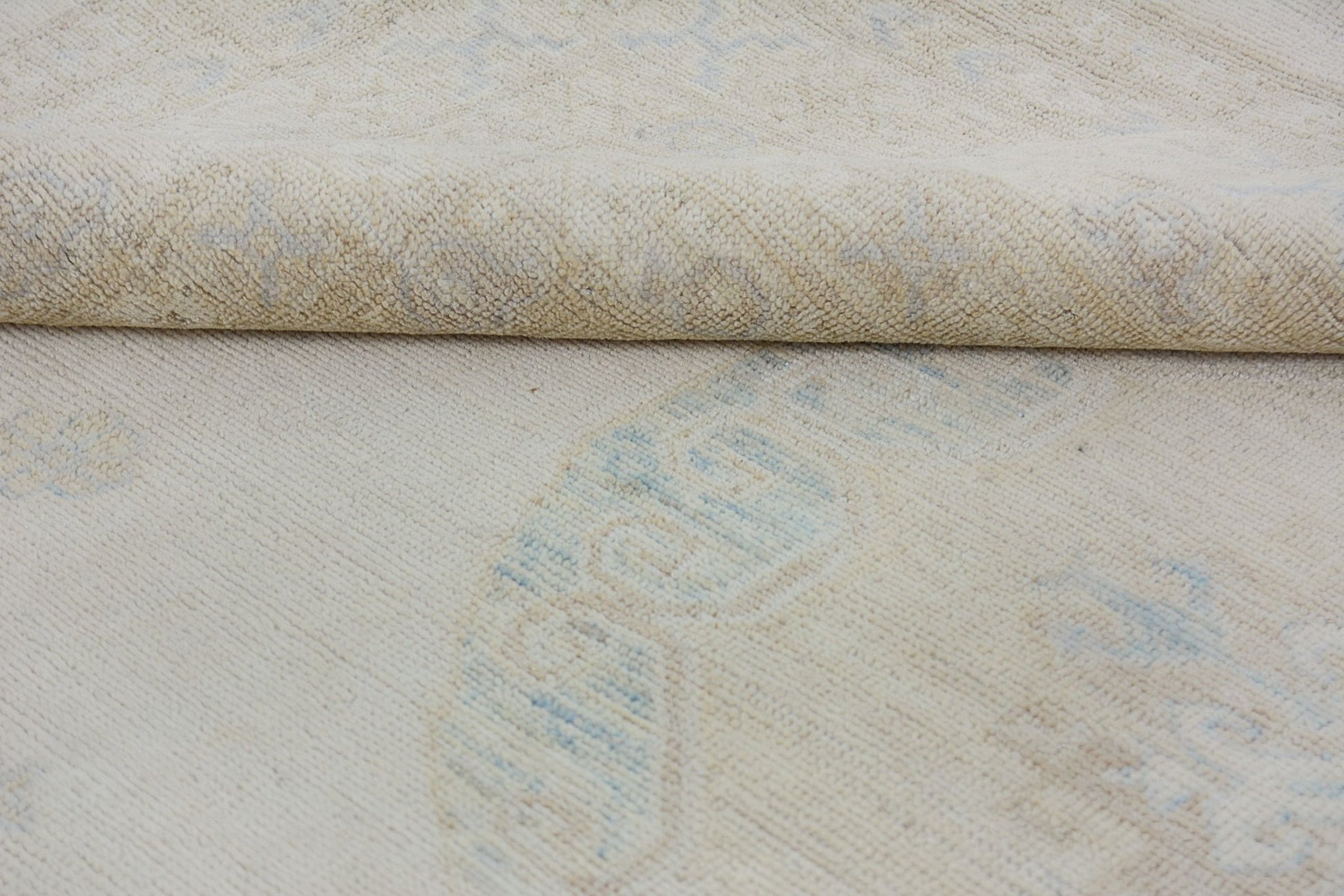 A close-up of a handmade Afghan Chobi rug featuring a light beige wool pile with blue patterns.