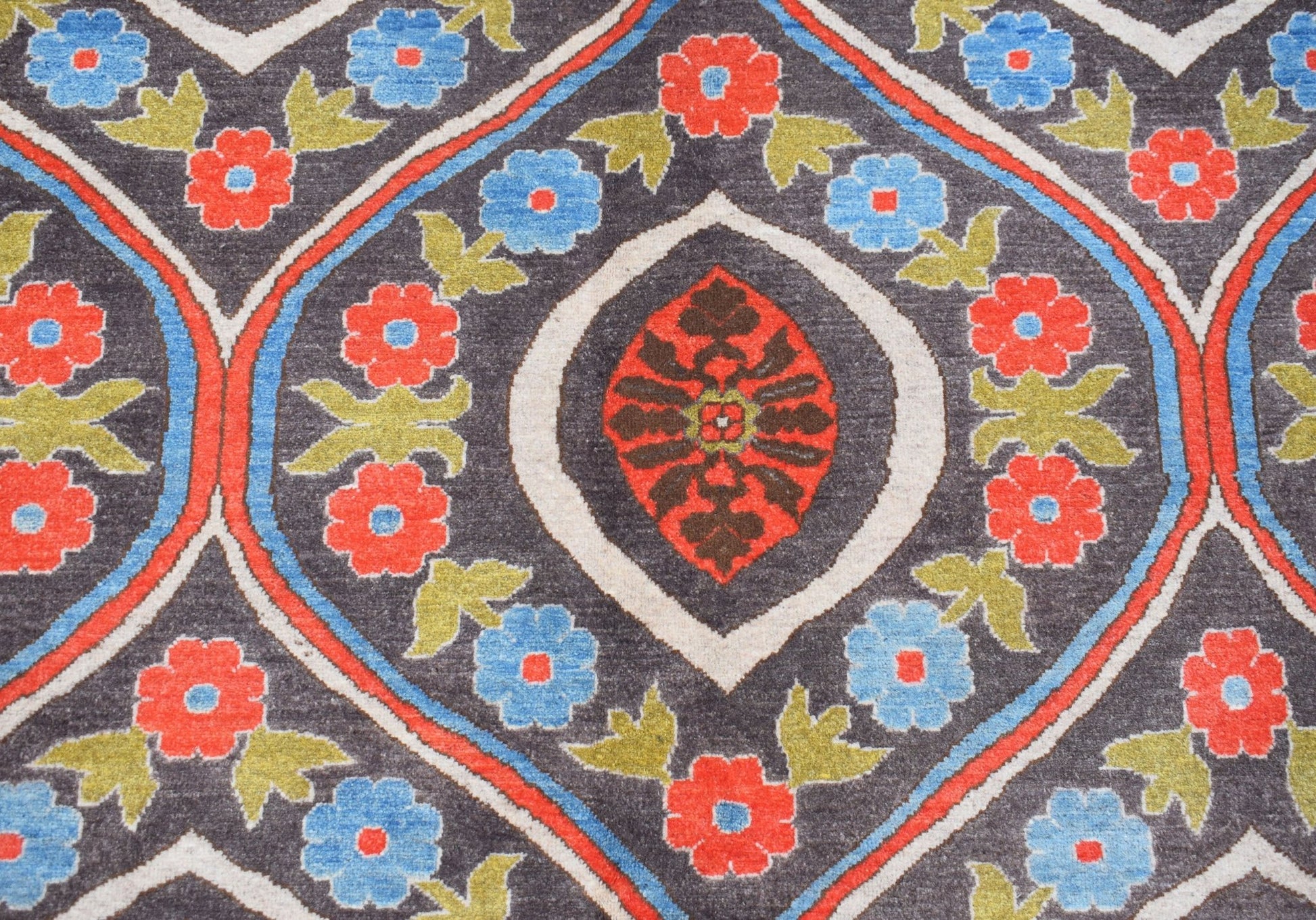 A handwoven Afghan Chobi rug featuring a repeating floral pattern in red, blue, and green on grey.