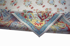 A handwoven Afghan Chobi rug with a cream field and a vibrant floral border folded over.