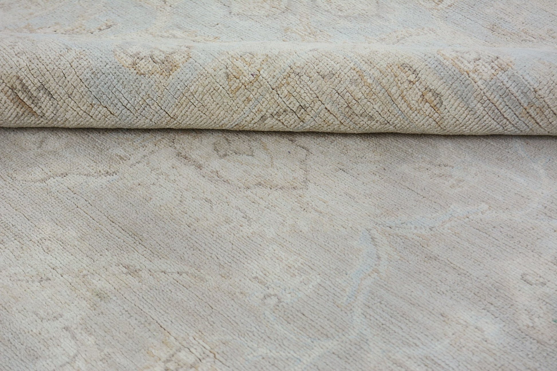 A close-up of a handmade Afghan Chobi rug in neutral tones with a folded corner.