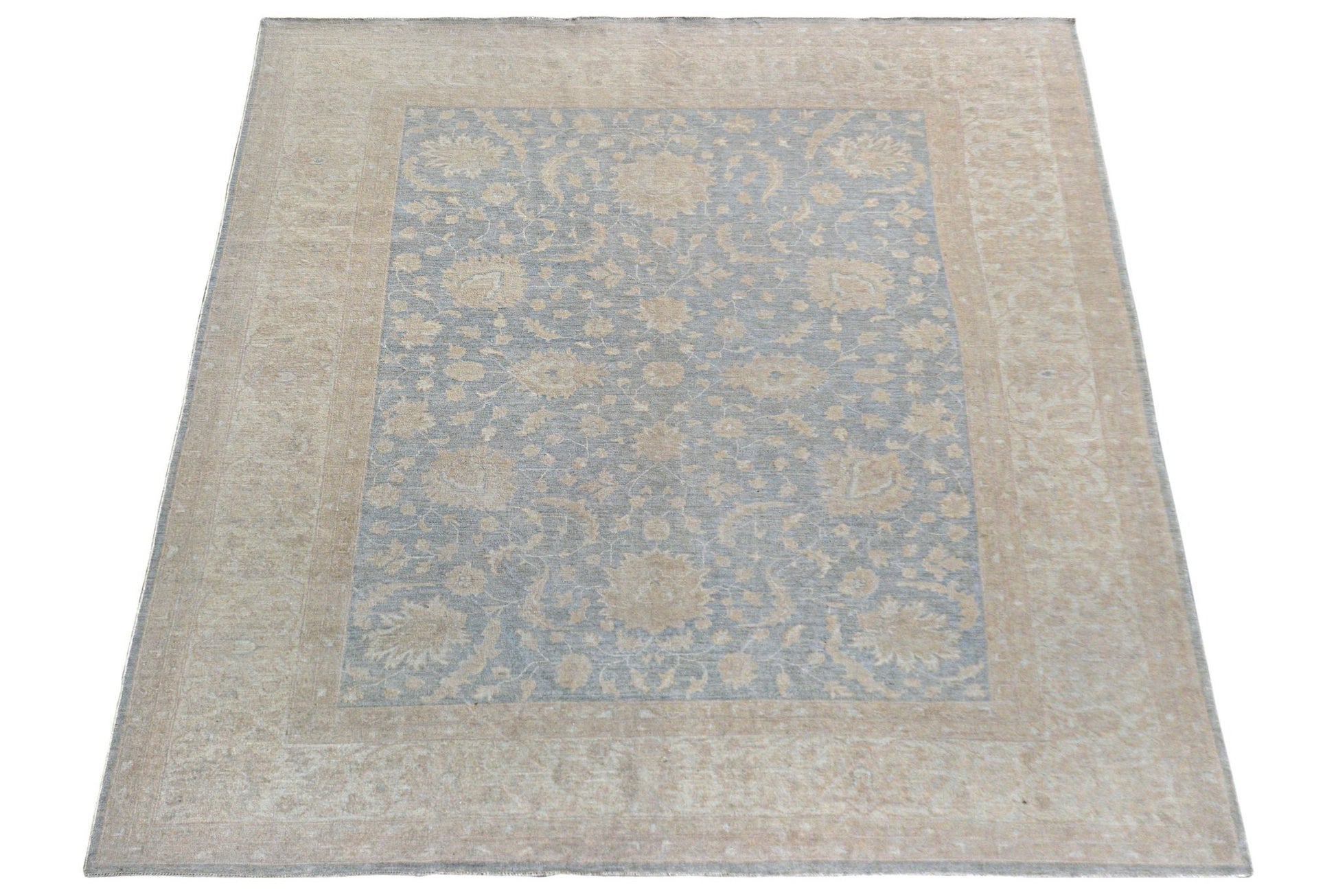 A handmade Afghan Chobi rug featuring a light blue central field with beige floral patterns.