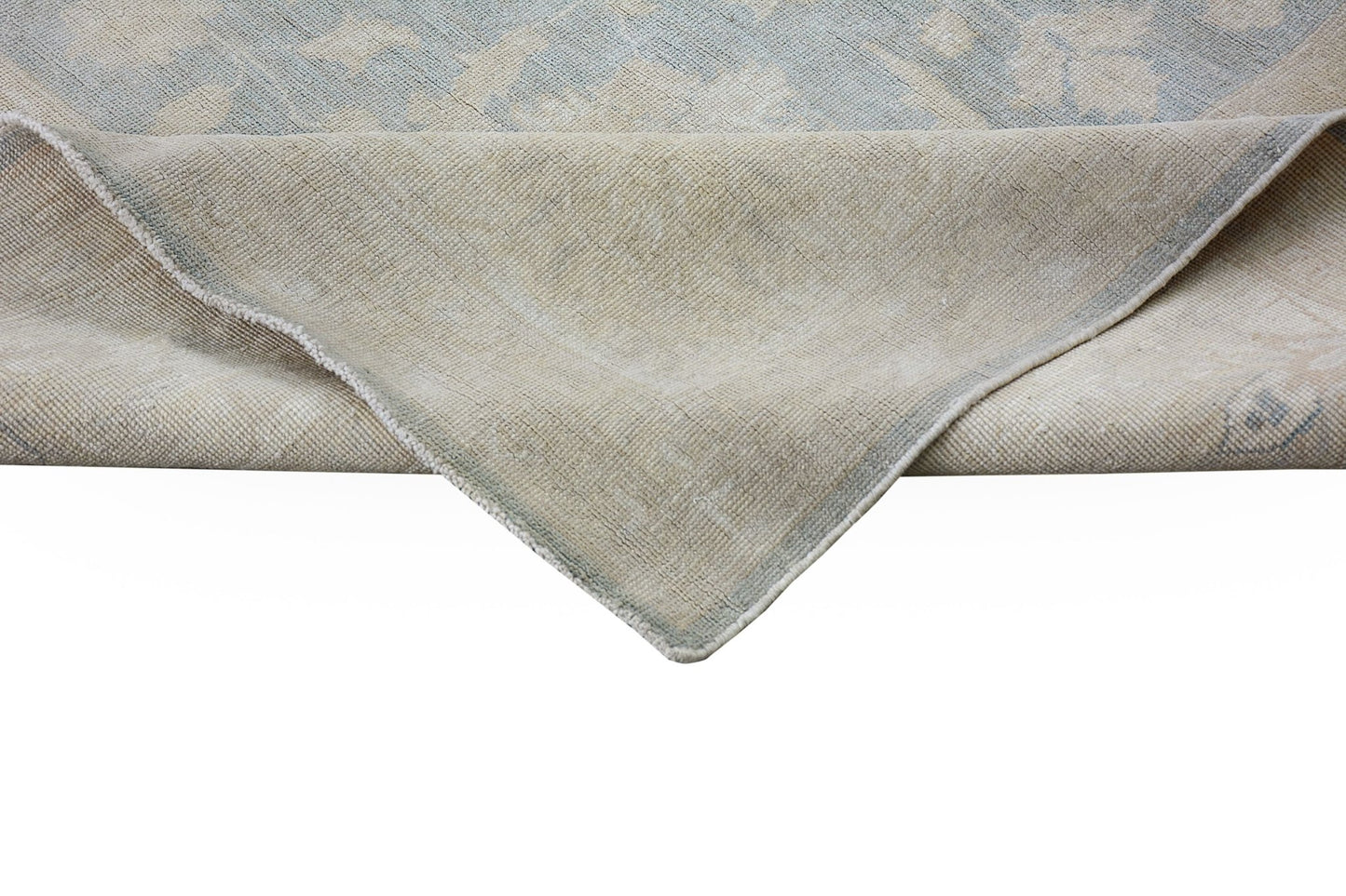 A corner of a handmade Afghan Chobi rug showing its light blue and beige wool pile and backing.
