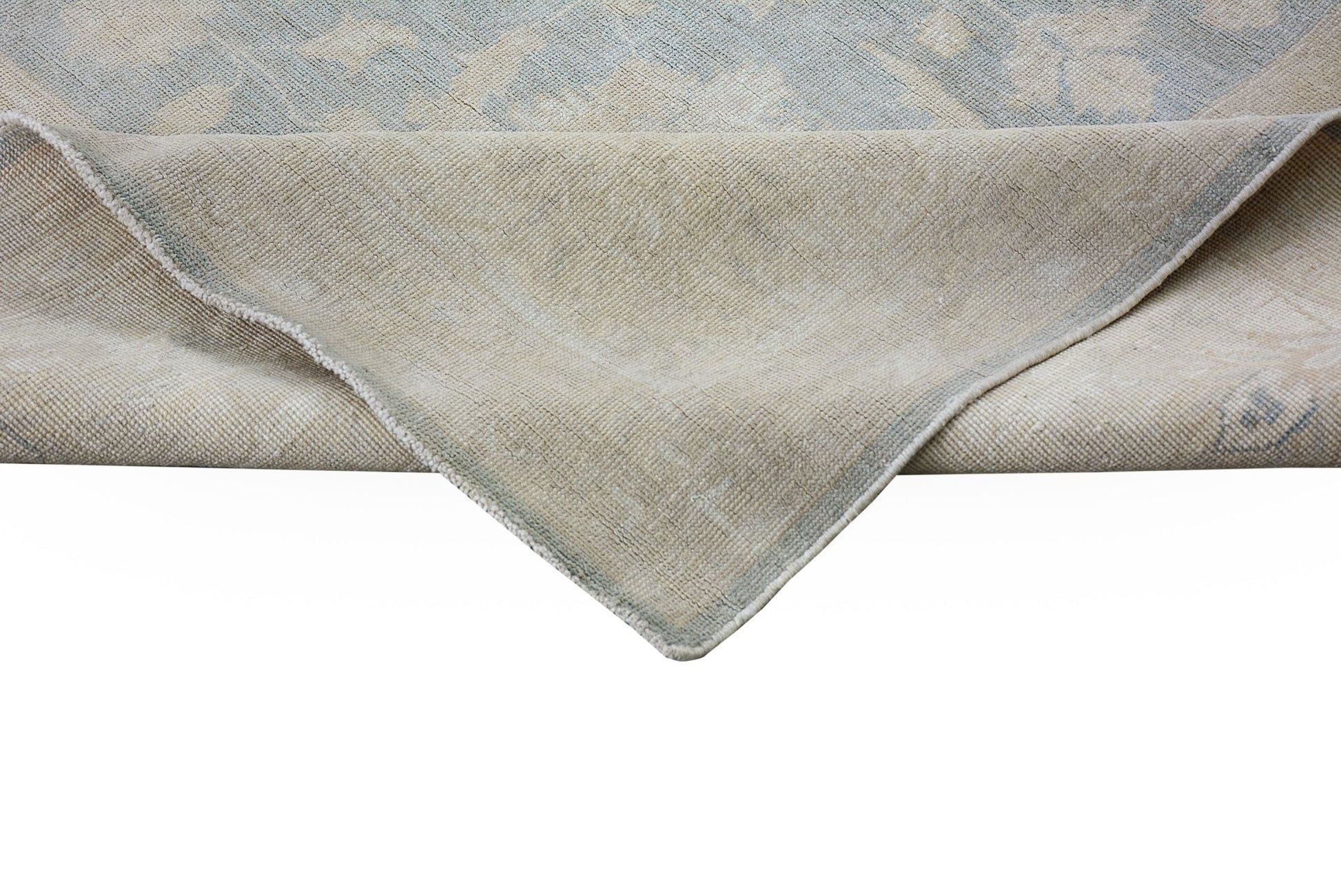 A corner of a handmade Afghan Chobi rug showing its light blue and beige wool pile and backing.