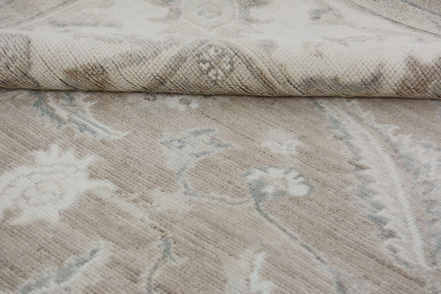 A close-up of a handmade Afghan Chobi rug featuring a neutral floral pattern and a folded corner.