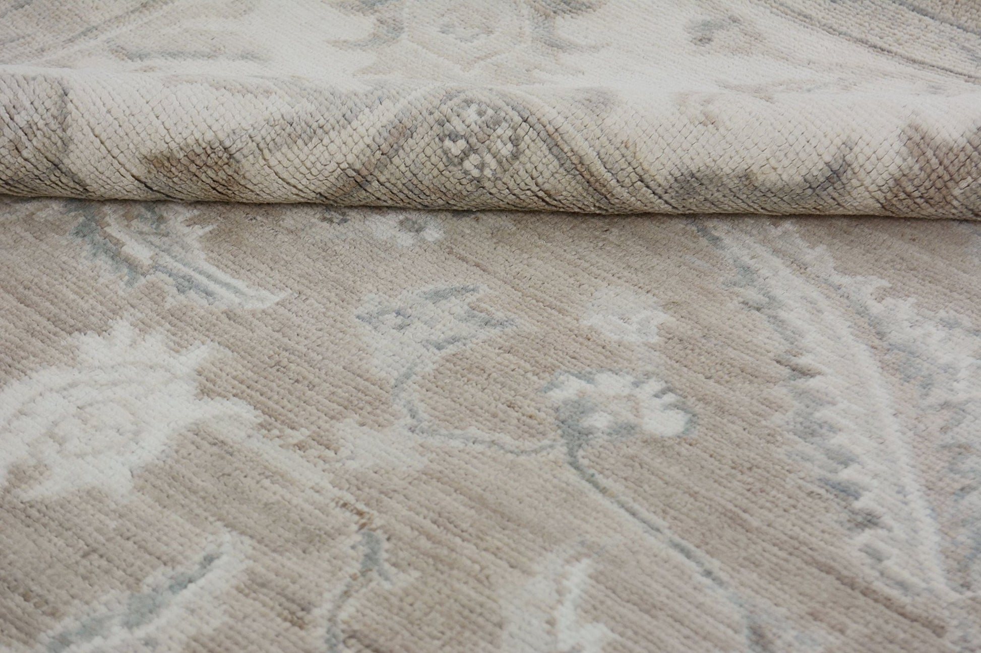 A close-up of a handmade Afghan Chobi rug featuring a neutral floral pattern and a folded corner.