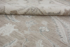 A close-up of a handmade Afghan Chobi rug featuring a neutral floral pattern and a folded corner.