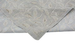A handmade Afghan Chobi rug featuring a light grey floral pattern with a folded corner.