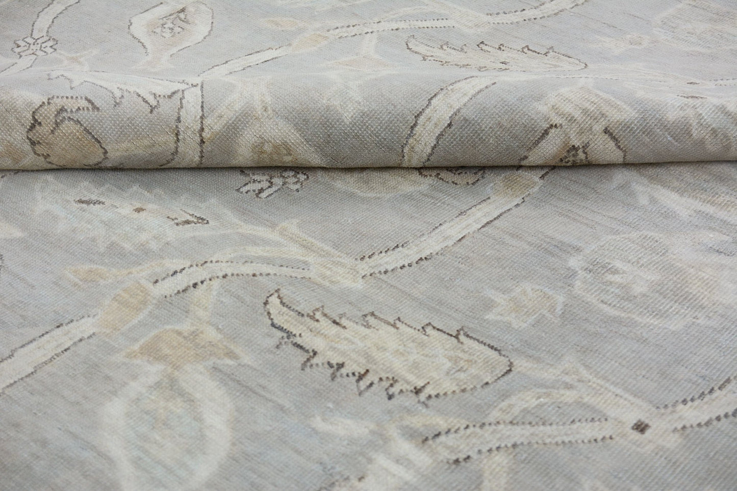 A handmade Afghan Chobi rug featuring a light grey and beige floral pattern on a wool pile.