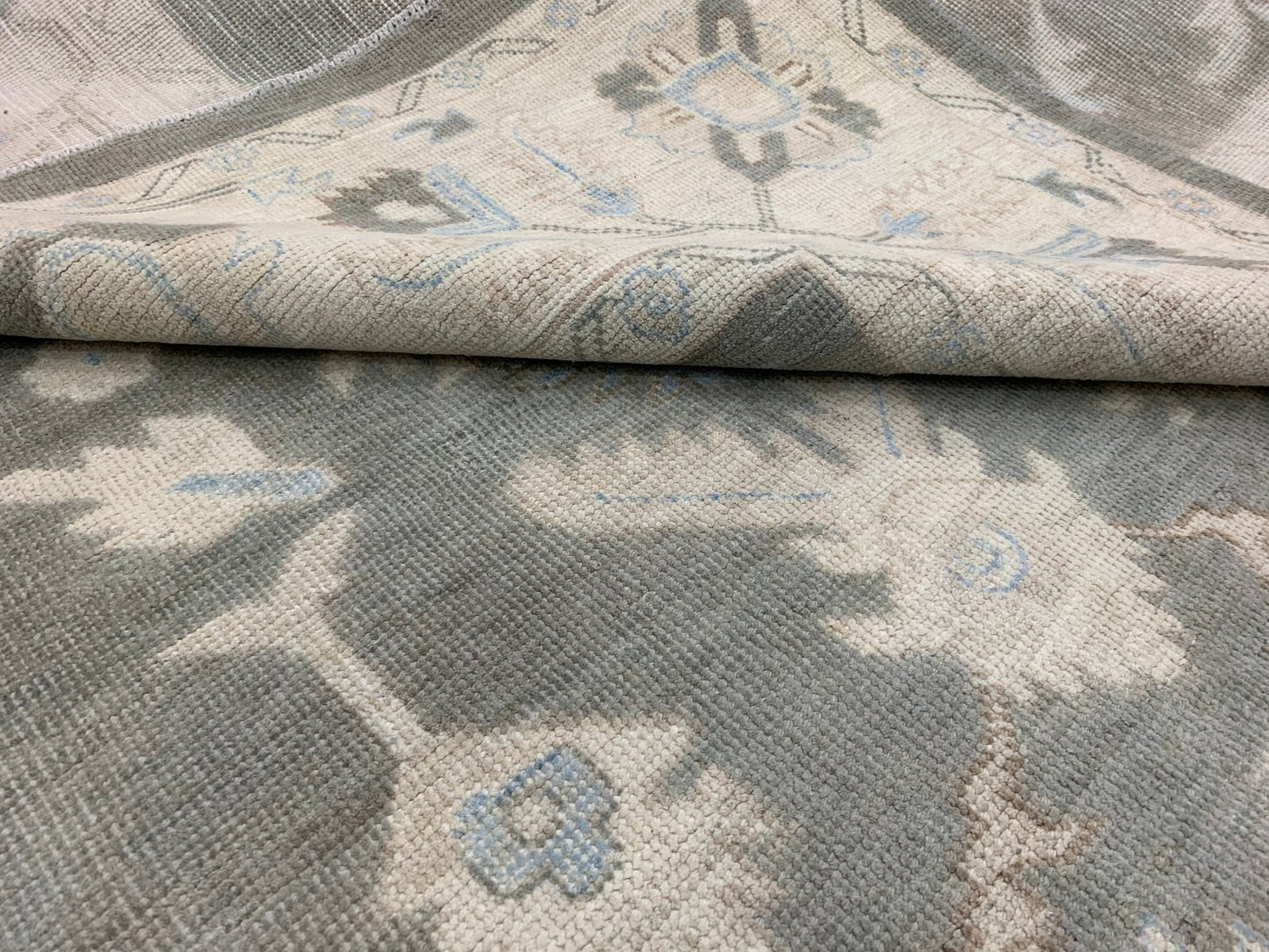 A handmade Afghan Chobi rug featuring a traditional floral pattern in shades of grey and blue.