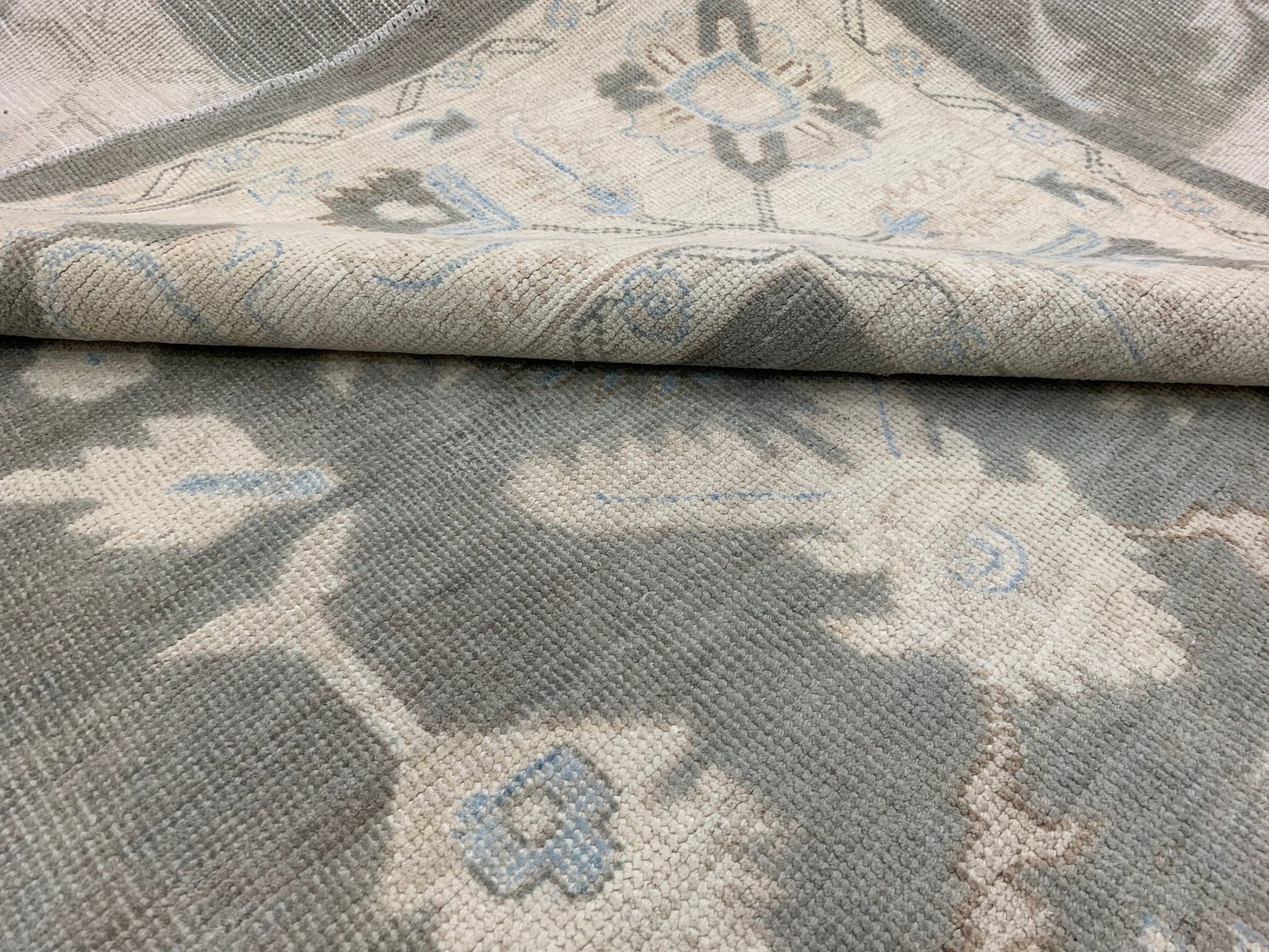 A handmade Afghan Chobi rug featuring a traditional floral pattern in shades of grey and blue.
