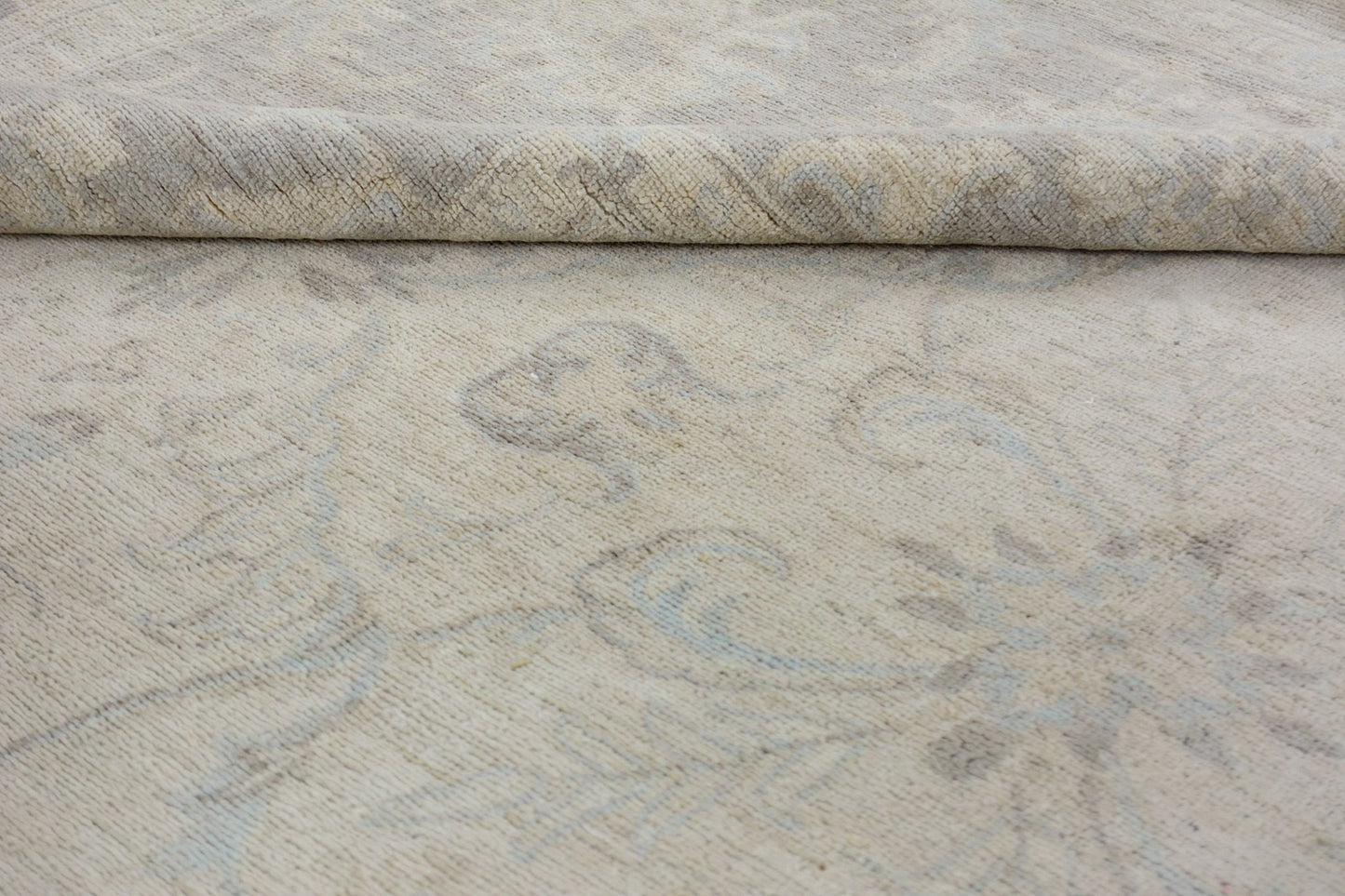 A close-up of a handmade Afghan Chobi rug featuring a subtle, light-toned floral pattern.